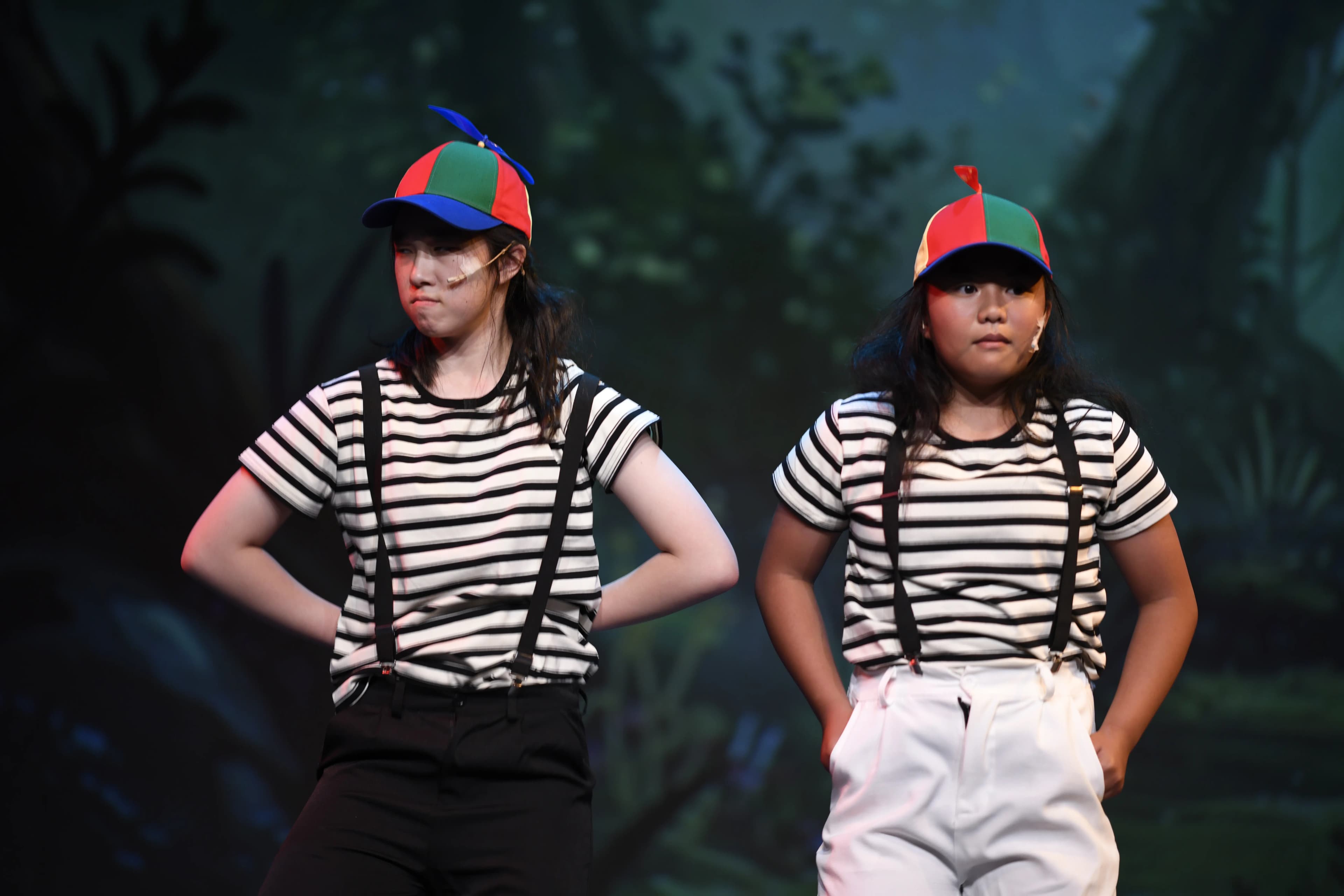 Two performers in striped shirts and colorful caps act onstage.
