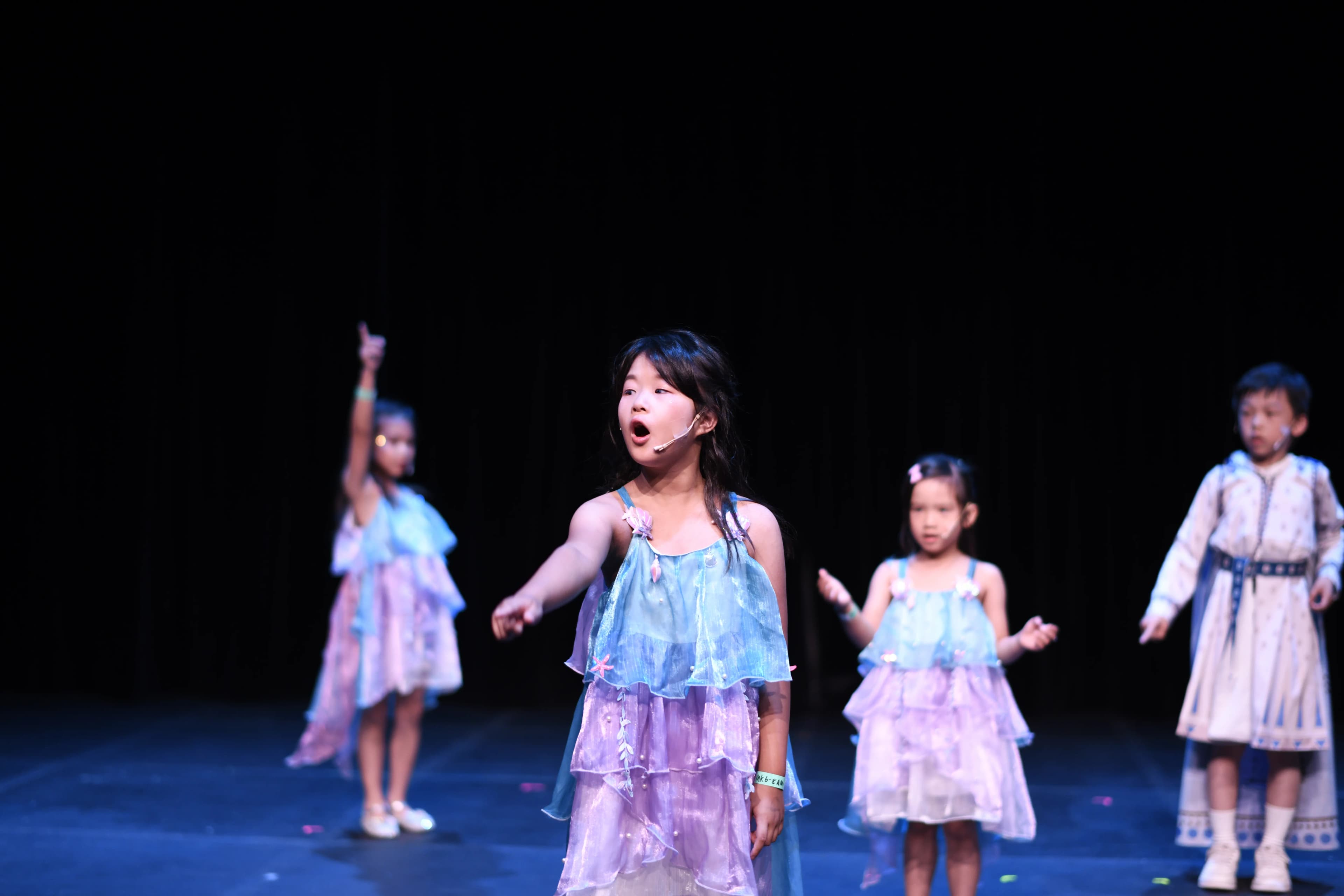 Four young TADA performers sing onstage in blue-and-purple costumes.