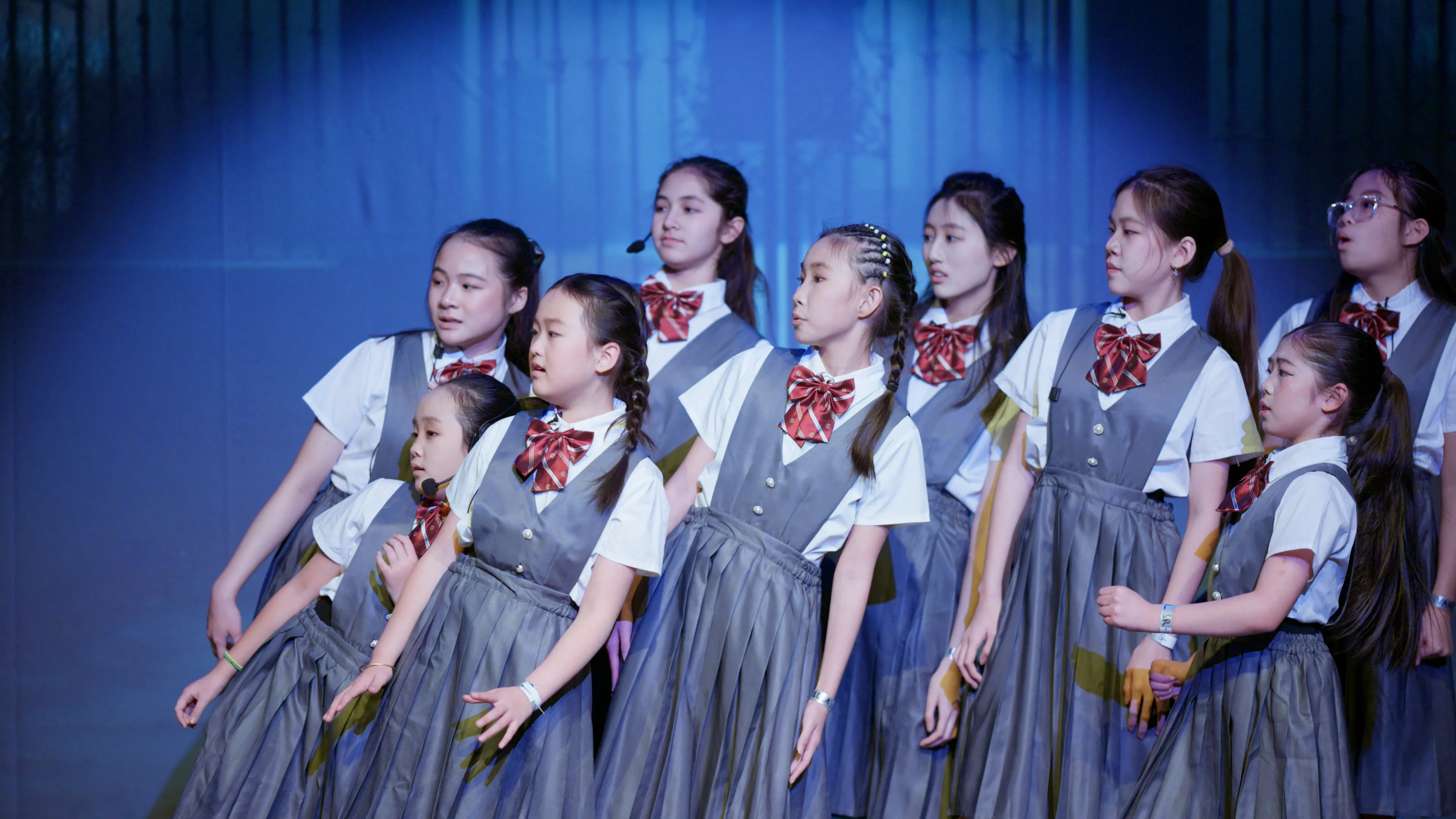 Students in school uniforms lean together during a dance number.
