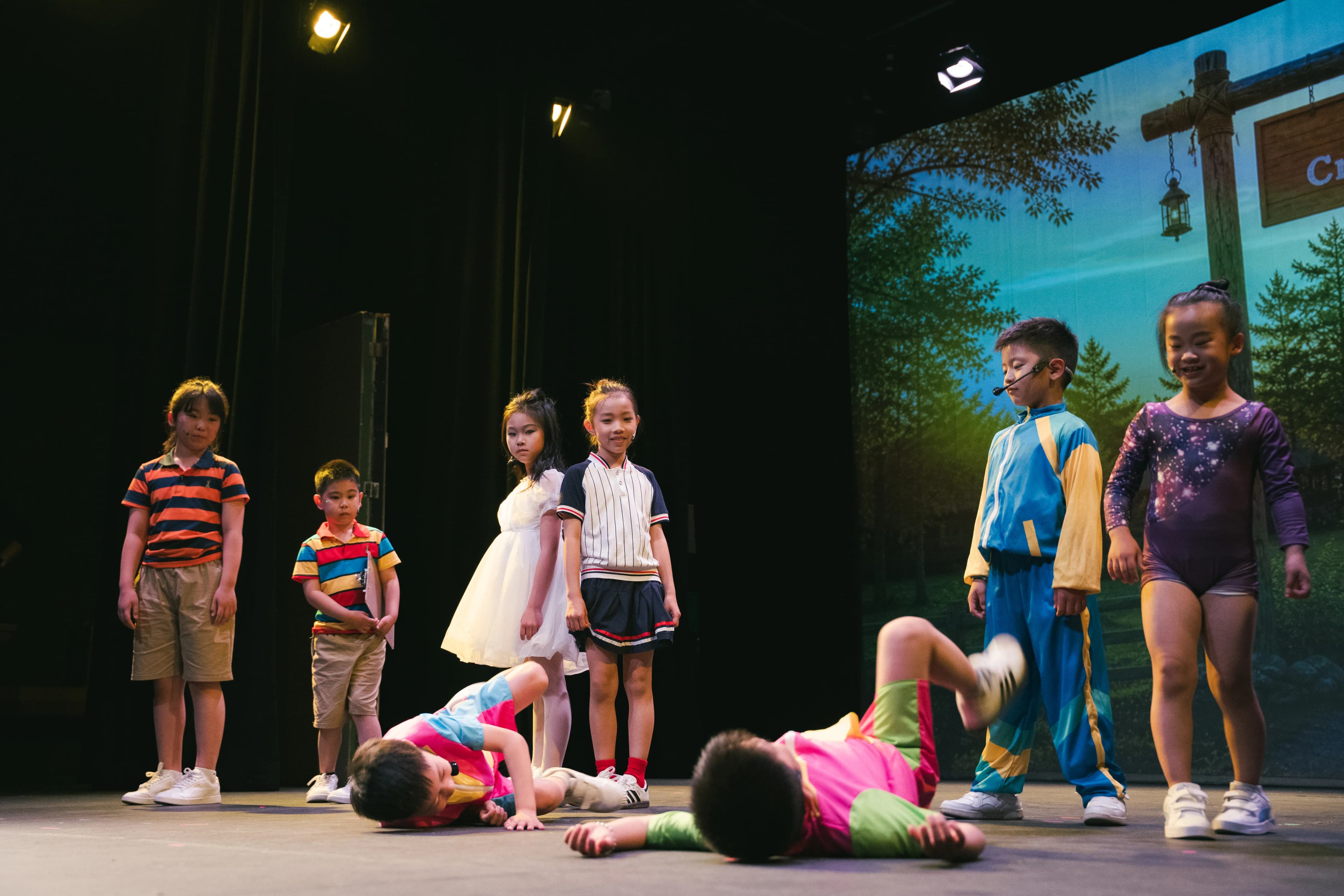 Young performers gather around a castmate lying onstage during a scene.