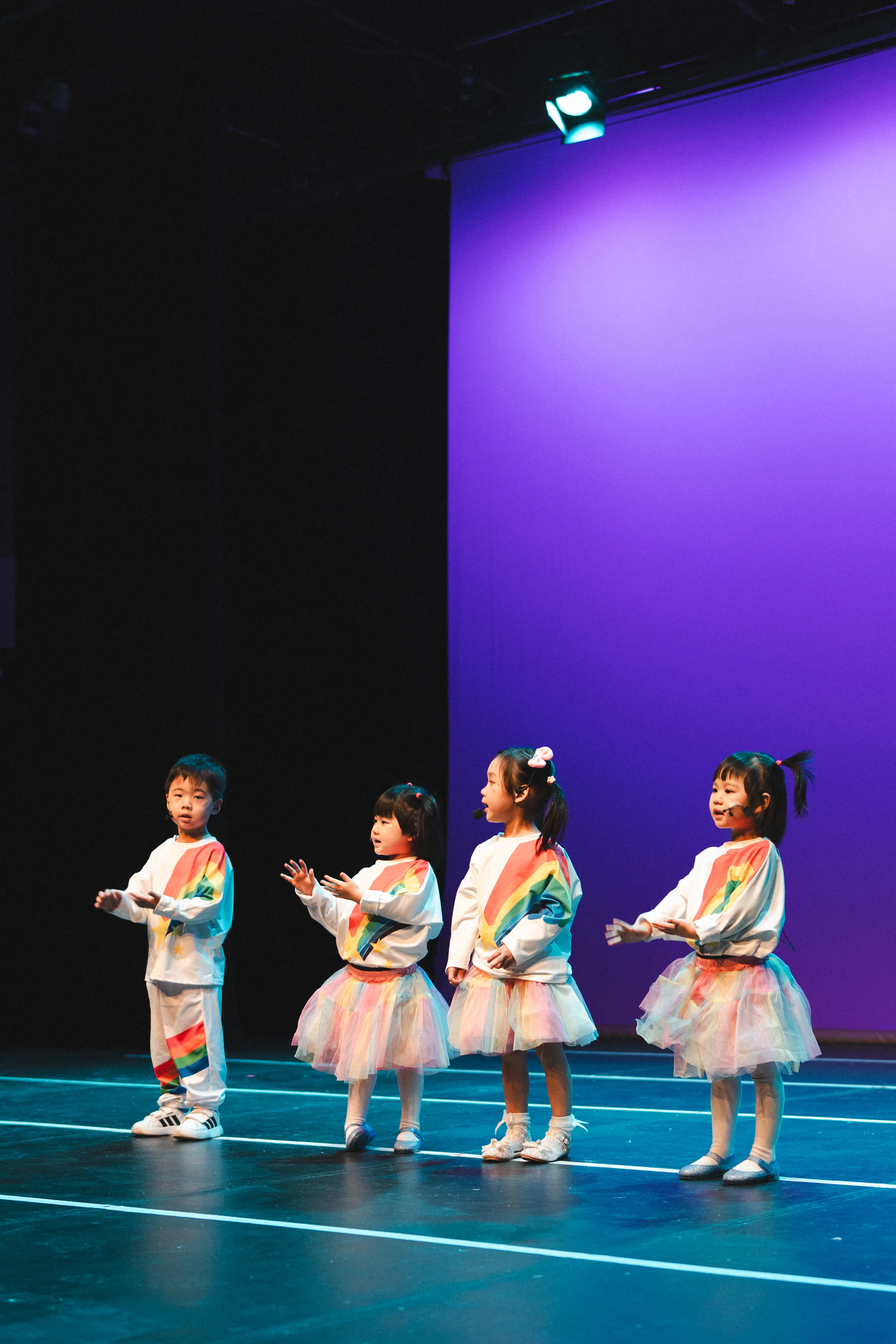 Four young performers in rainbow costumes dance together onstage.
