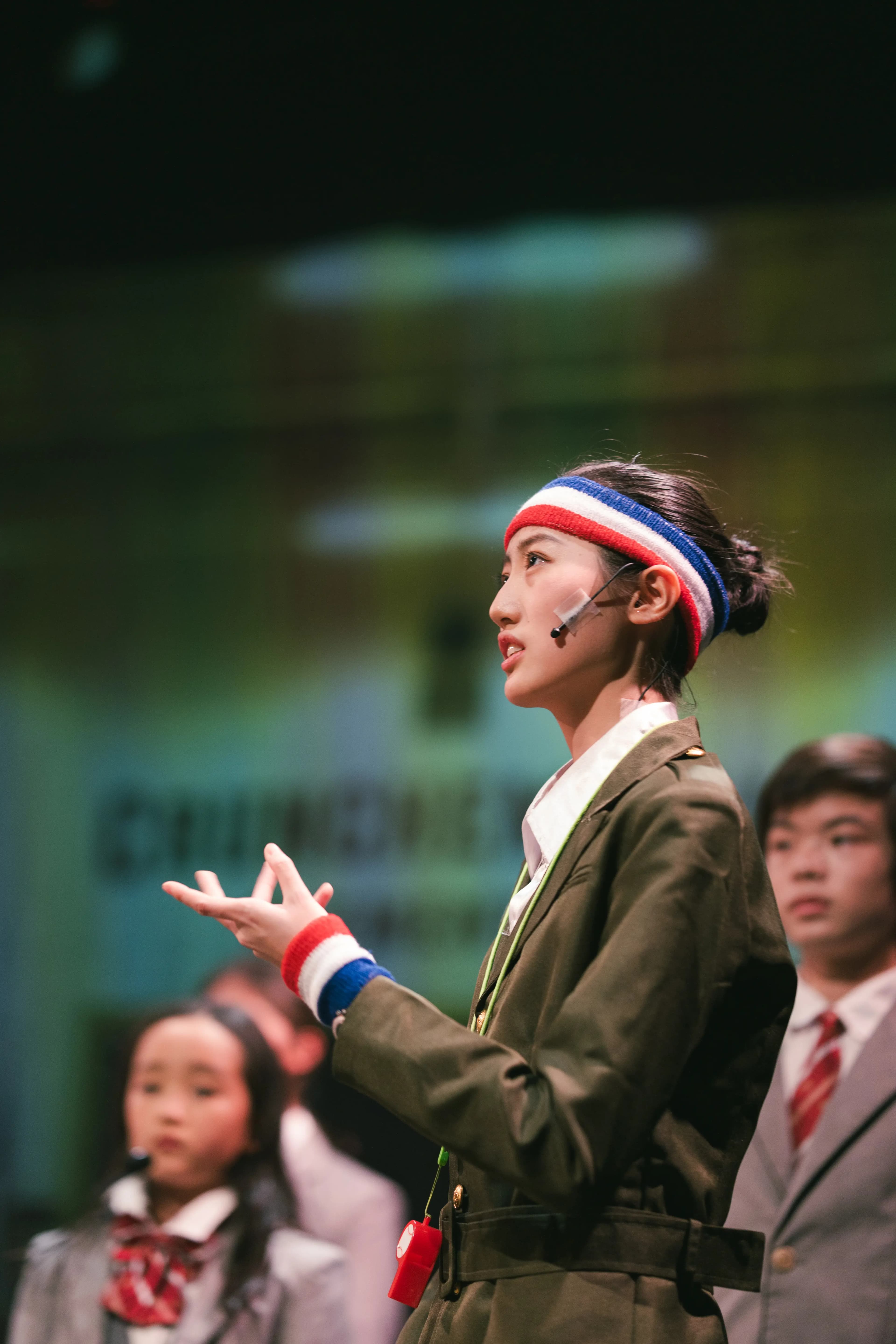 A Senior Troupe performer delivers a speech in a school uniform and headband.