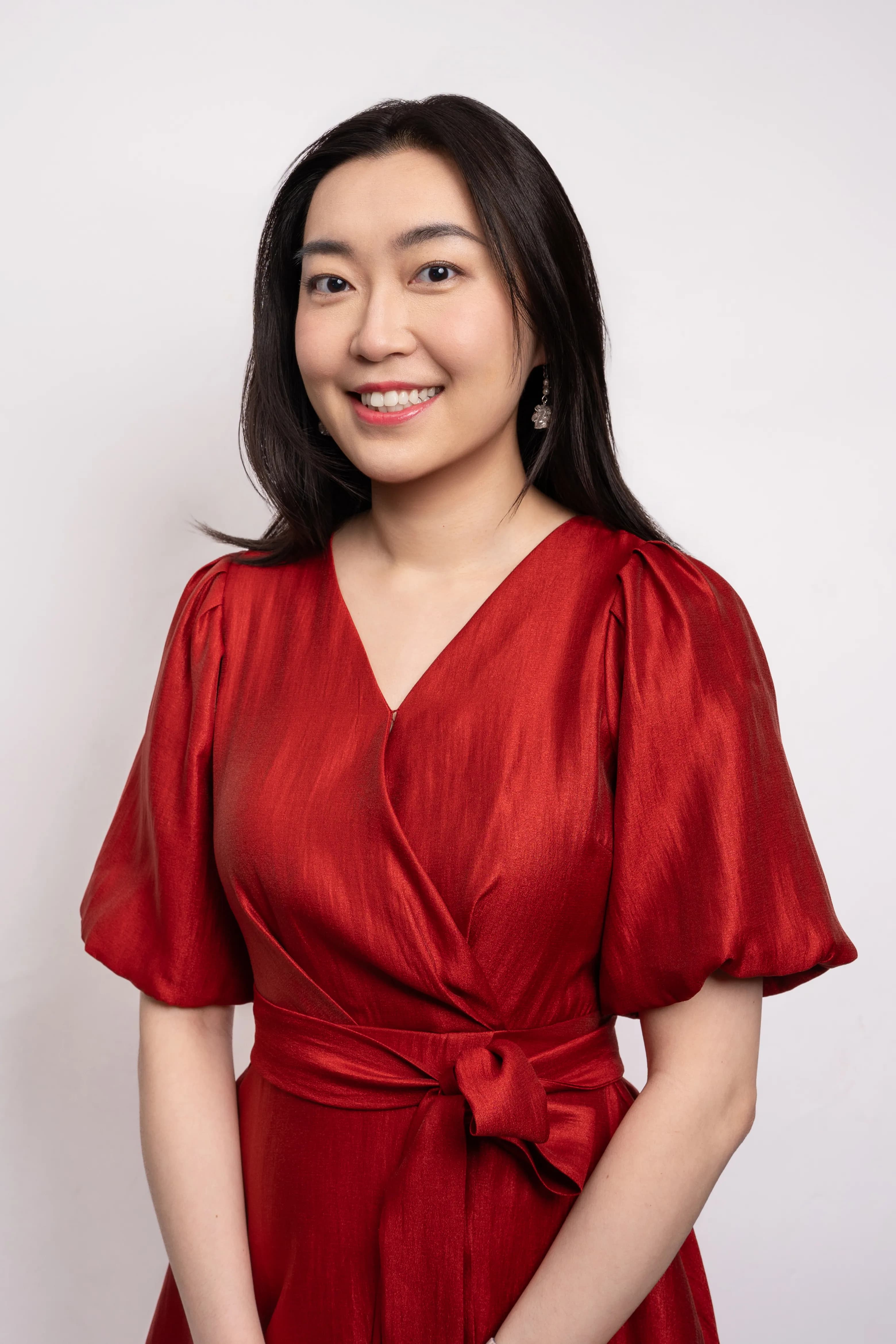 A professional headshot of the founder and director, who is smiling and wearing an elegant, red dress.