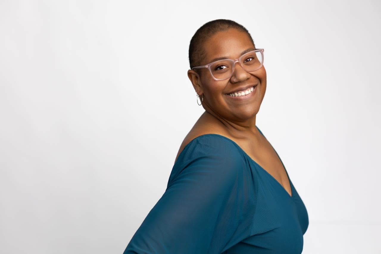 A professional headshot of a teacher, wearing a silky dark blue blouse.
